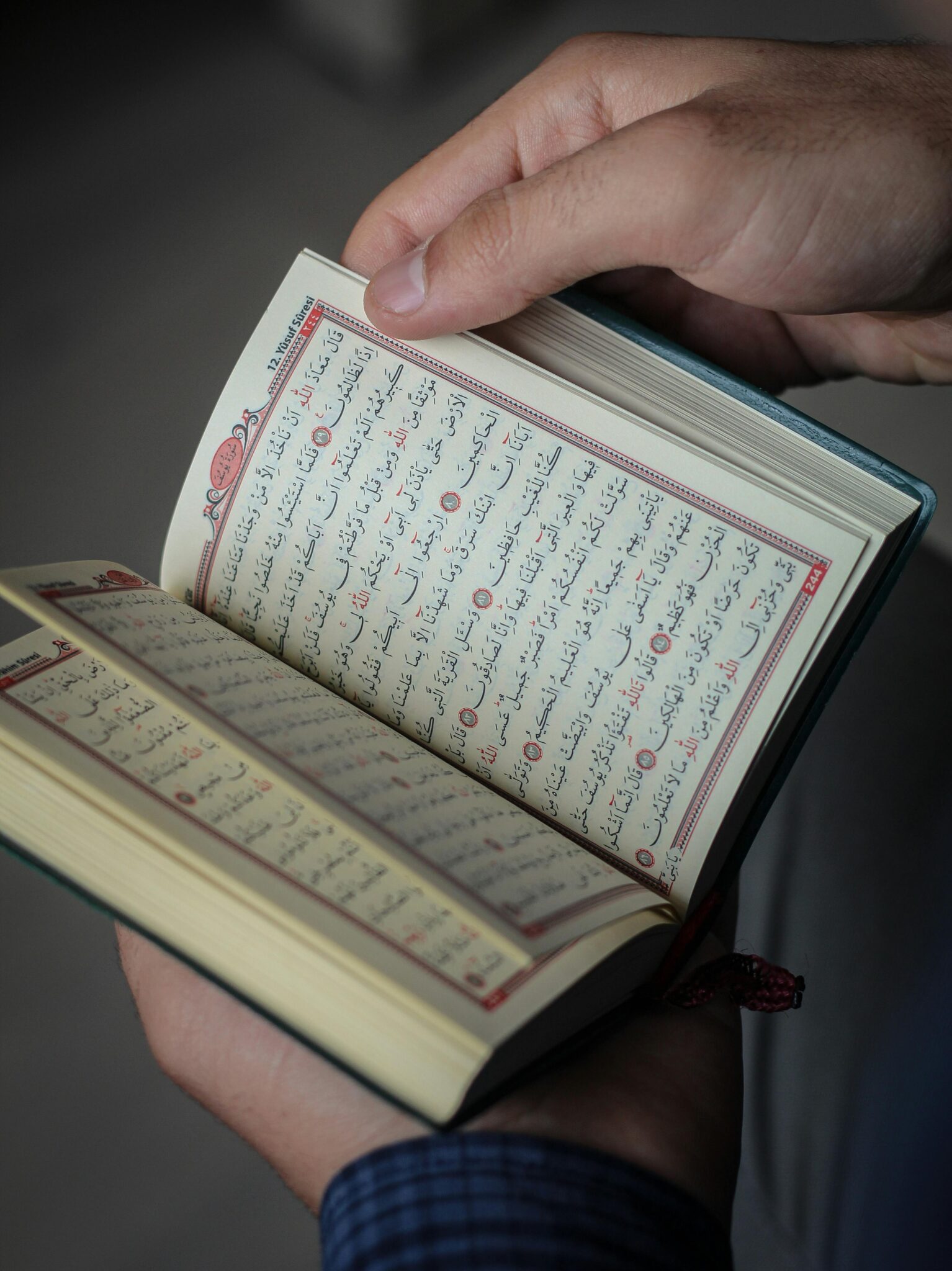 Close-up of hands holding an open Quran, showcasing intricate Arabic script and religious devotion.